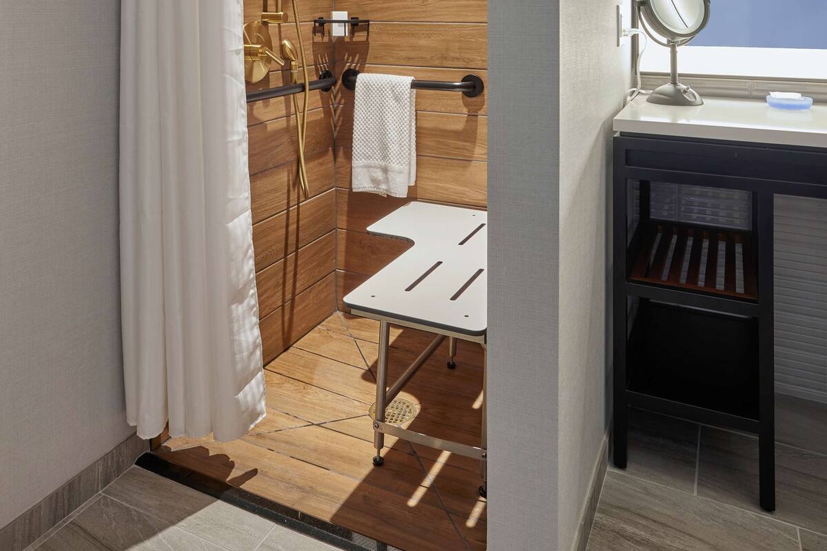 A modern bathroom with a wooden panel wall, a shower with a gold showerhead, a small white sink with a mirror, and a towel rack.