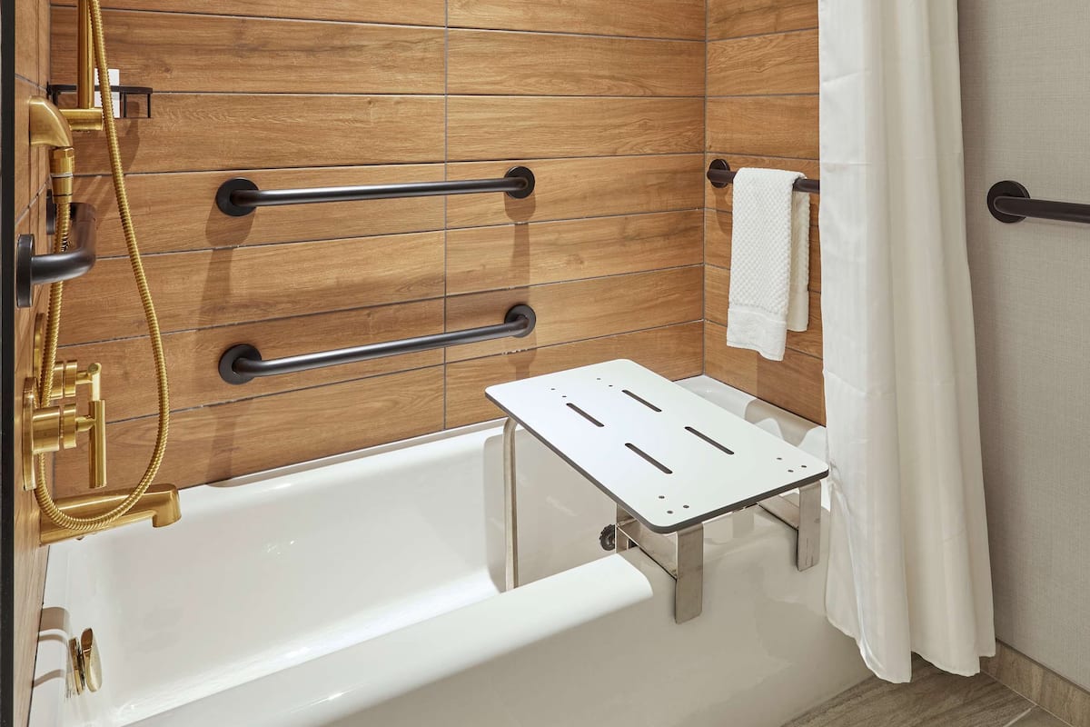 A modern bathroom with a wooden panel wall, a white bathtub, a gold showerhead, and a white shower curtain.