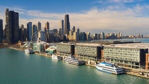 Un paisaje urbano frente al agua con edificios modernos, una noria y varios cruceros amarrados.