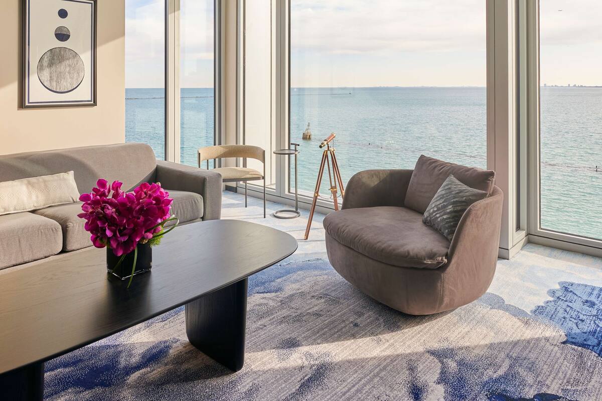 A modern living room with a large window overlooking a body of water, a tripod, and a sofa.