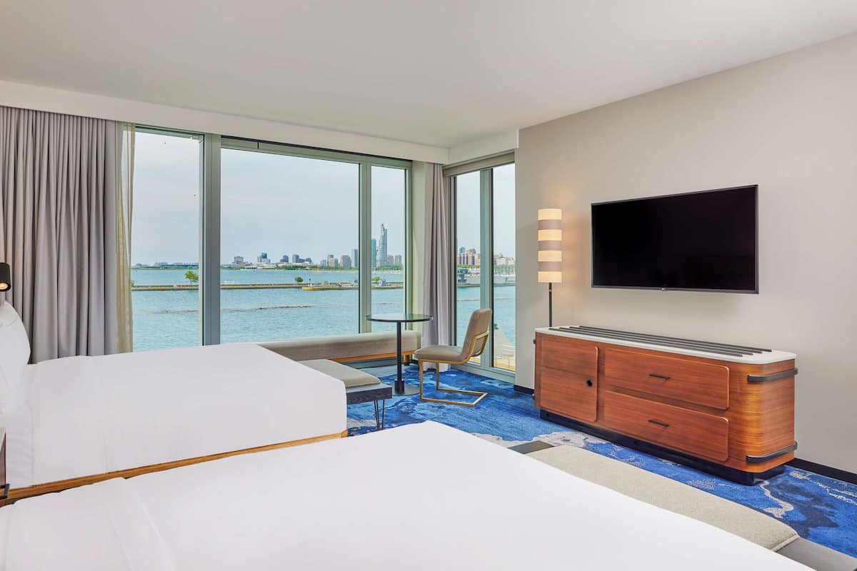 A hotel room with a bed, a desk, a chair, a TV, and a view of the city and water.