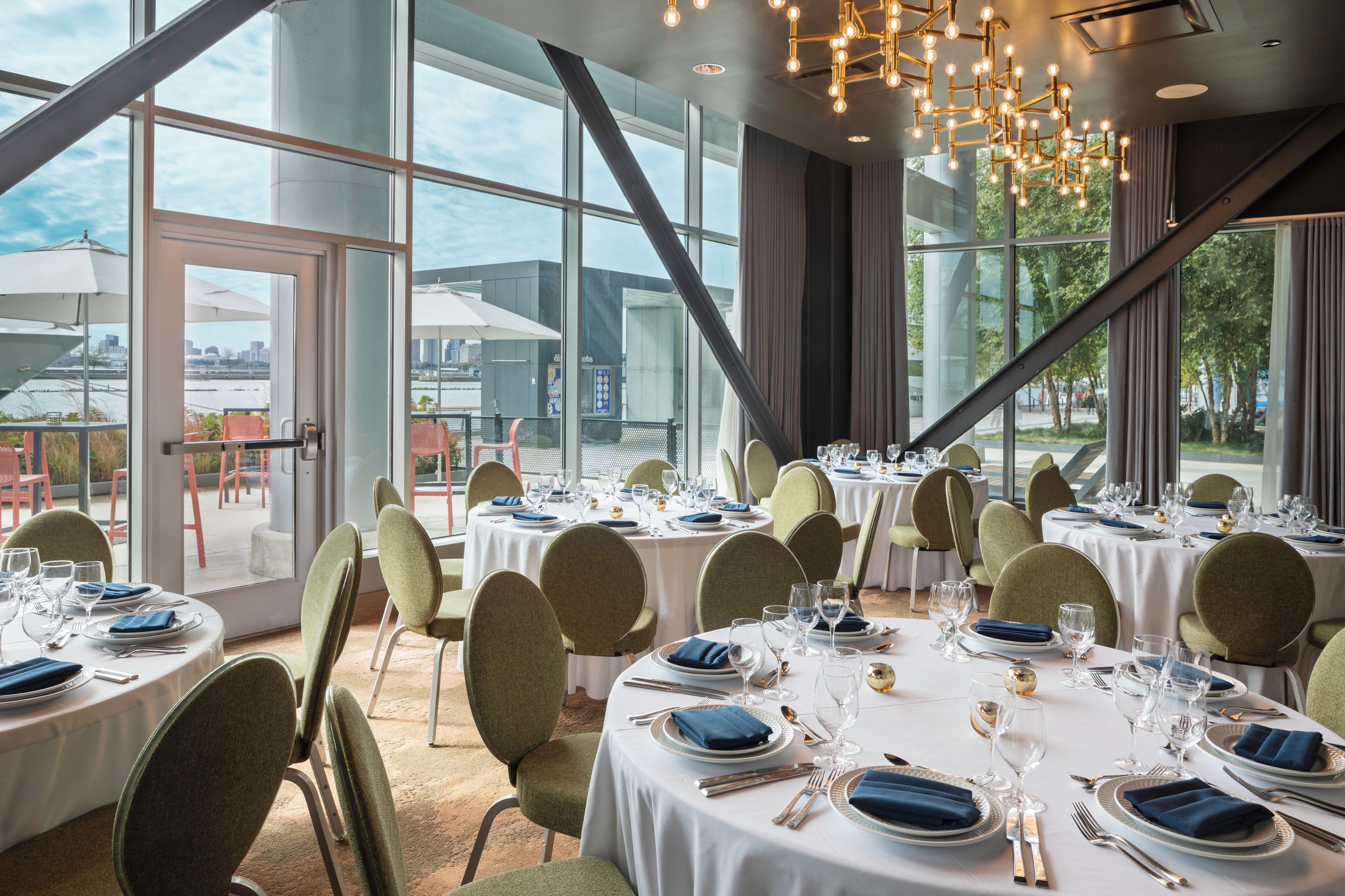 A restaurant with round tables set for dining, large windows, and a modern chandelier.