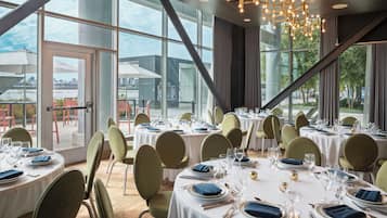 En restaurang med runda bord, stora fönster och en modern kristallkrona.