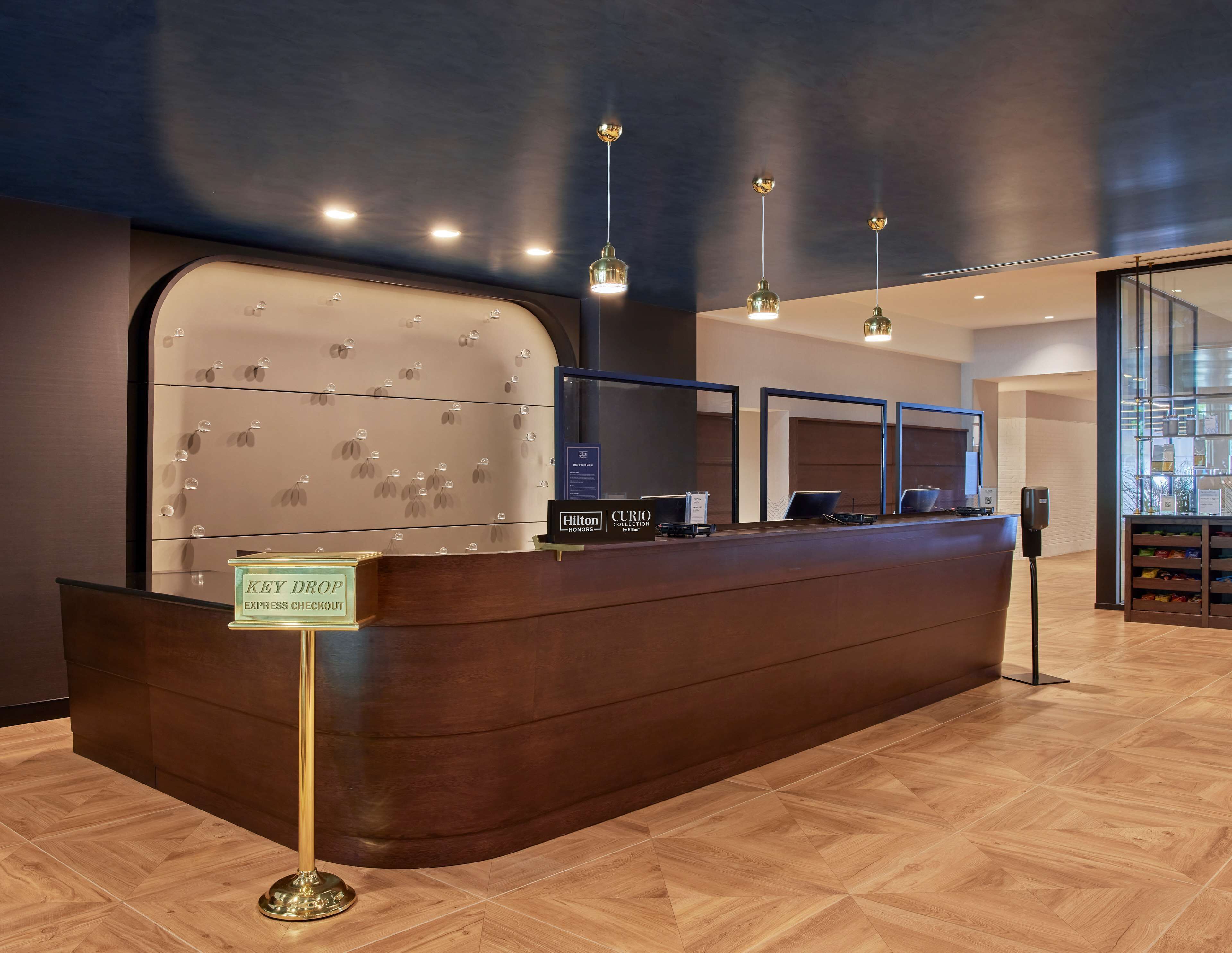 A hotel reception desk with a key drop and express check-out sign, a display of awards, and a modern interior with wooden flooring and pendant lighting.