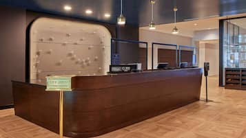 A hotel reception desk with a key drop and express check-out sign, a display of awards, and a modern interior with wooden flooring and pendant lighting.