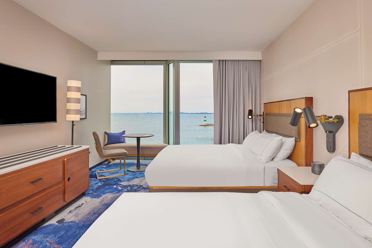 A hotel room with a large bed, a TV, a desk, and a view of the sea.