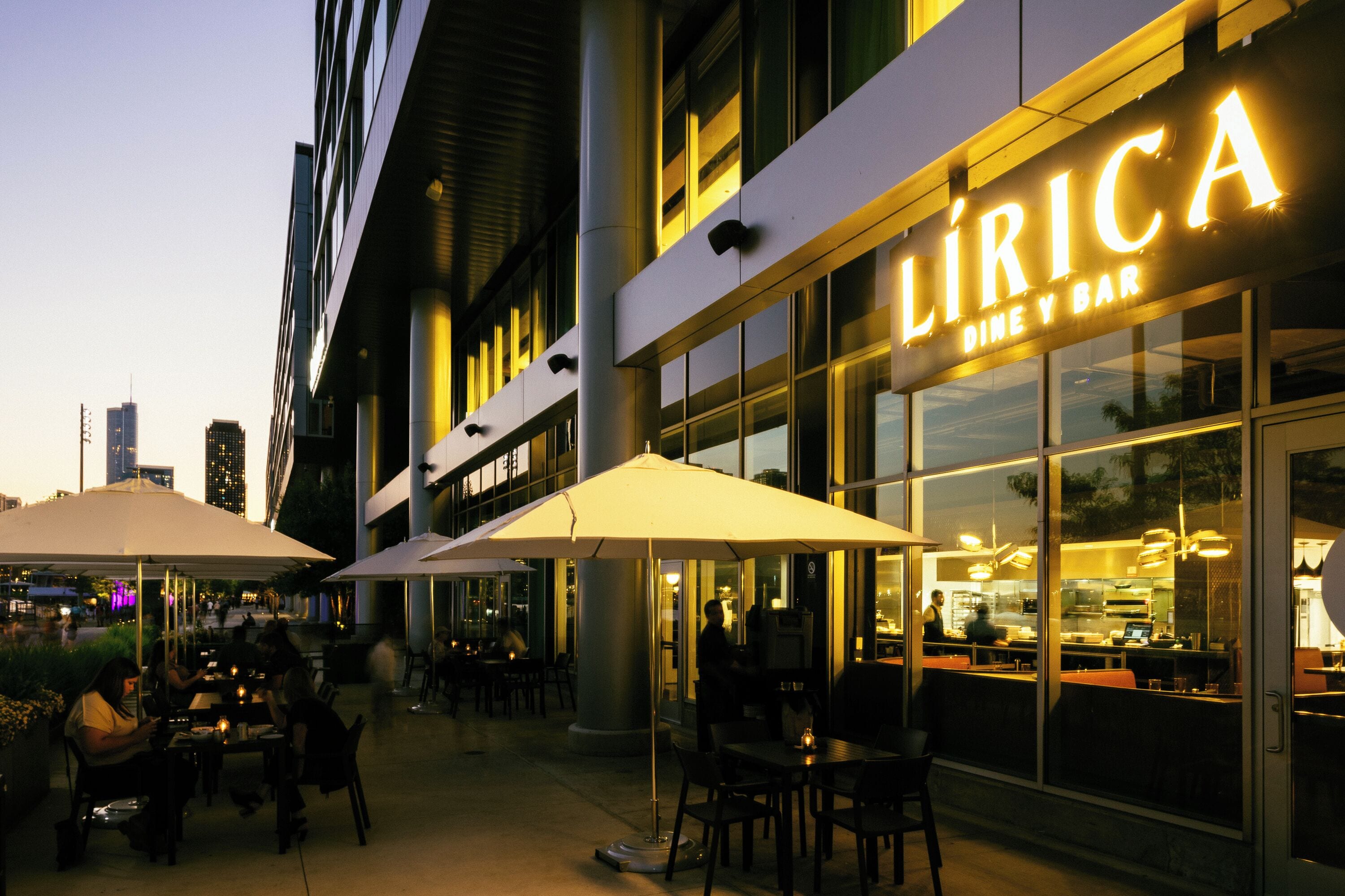 Un área de comedor al aire libre con mesas y sombrillas en un restaurante llamado LIRICA.