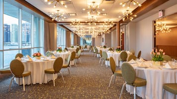 A banquet hall with round tables, chairs, and floral centerpieces.