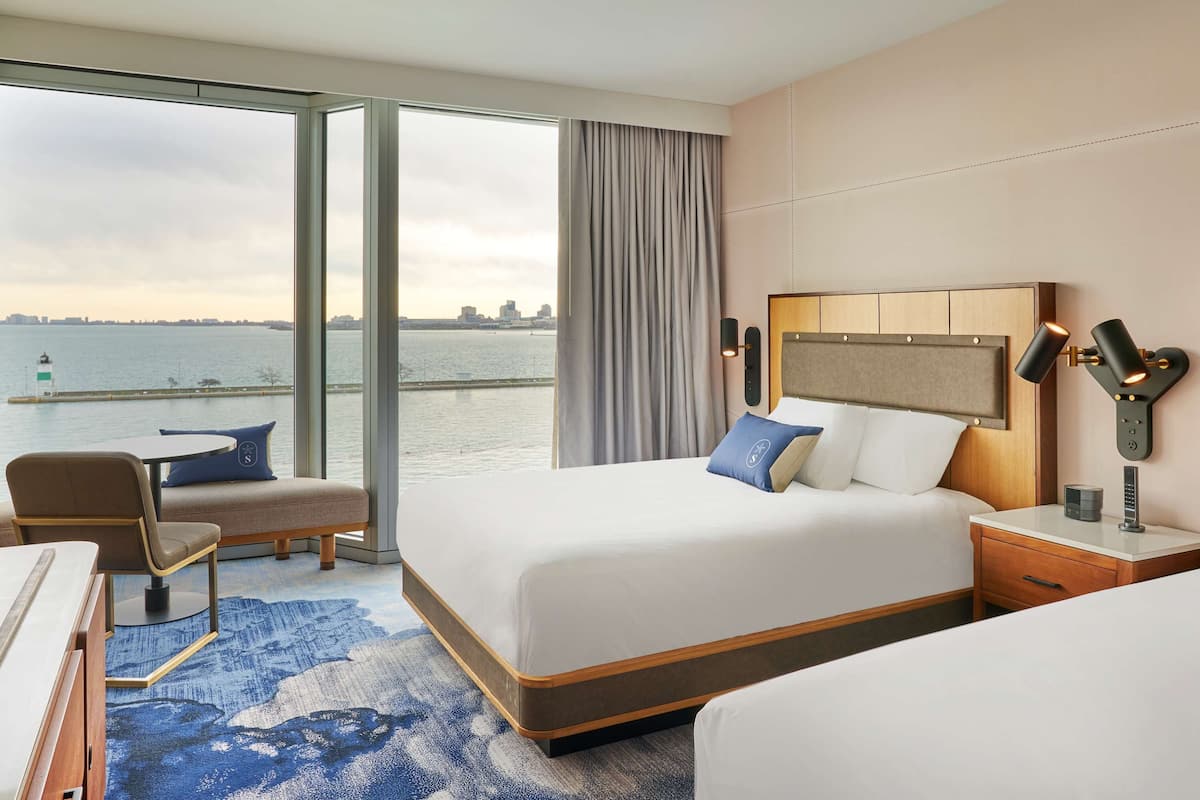A hotel room with two beds, a desk, a chair, and a view of the water.