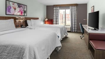 Une chambre d’hôtel avec deux lits, un bureau, une télévision et une fenêtre avec des rideaux.