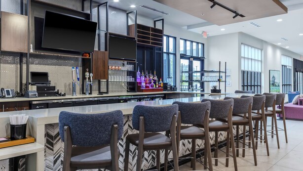A modern bar area with a flat-screen TV, bar stools, and a variety of bottles and glasses. - Hilton Garden Inn Detroit Utica (Clinton Township)