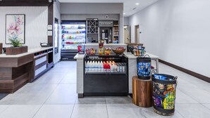 A clean, modern retail area with a refrigerated section, a variety of snacks, and a counter with a plant. - Hilton Garden Inn Detroit Utica (Clinton Township)
