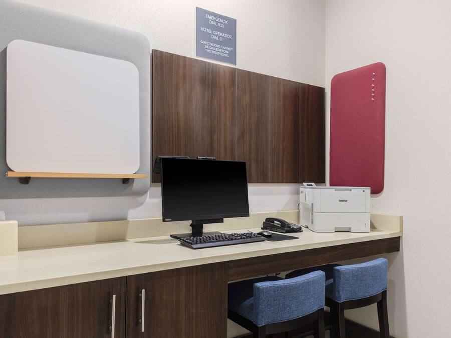 A hotel reception desk with a computer, telephone, and printer. There are two blue chairs and a whiteboard on the wall.