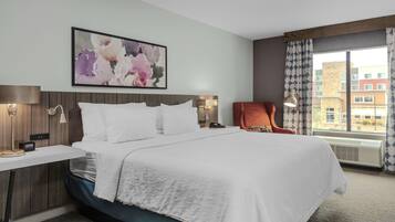 A hotel room with a large bed, a bedside table with a lamp, a chair, and a window with curtains.