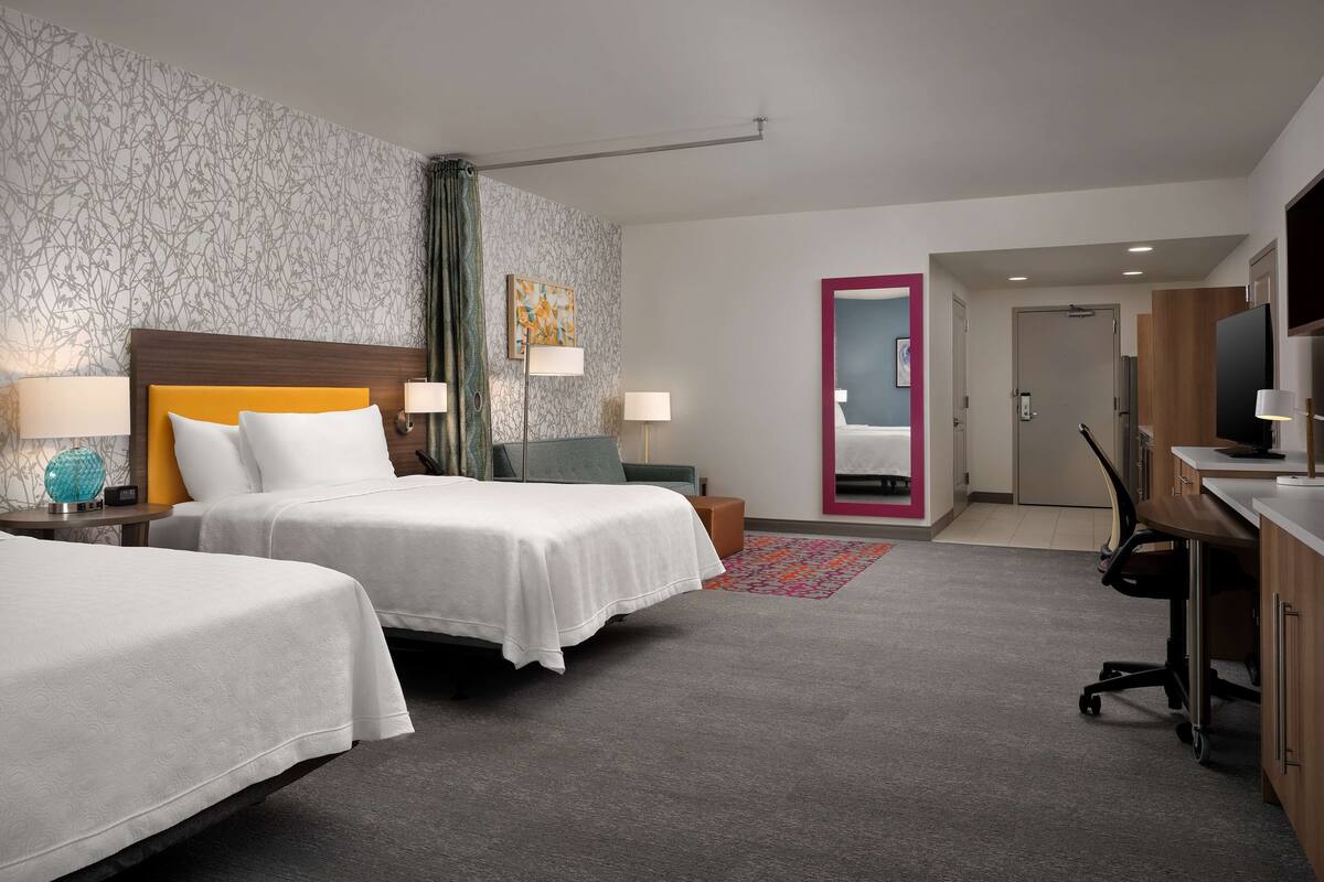 A hotel room with two beds, a desk, a chair, a TV, and a bathroom door.