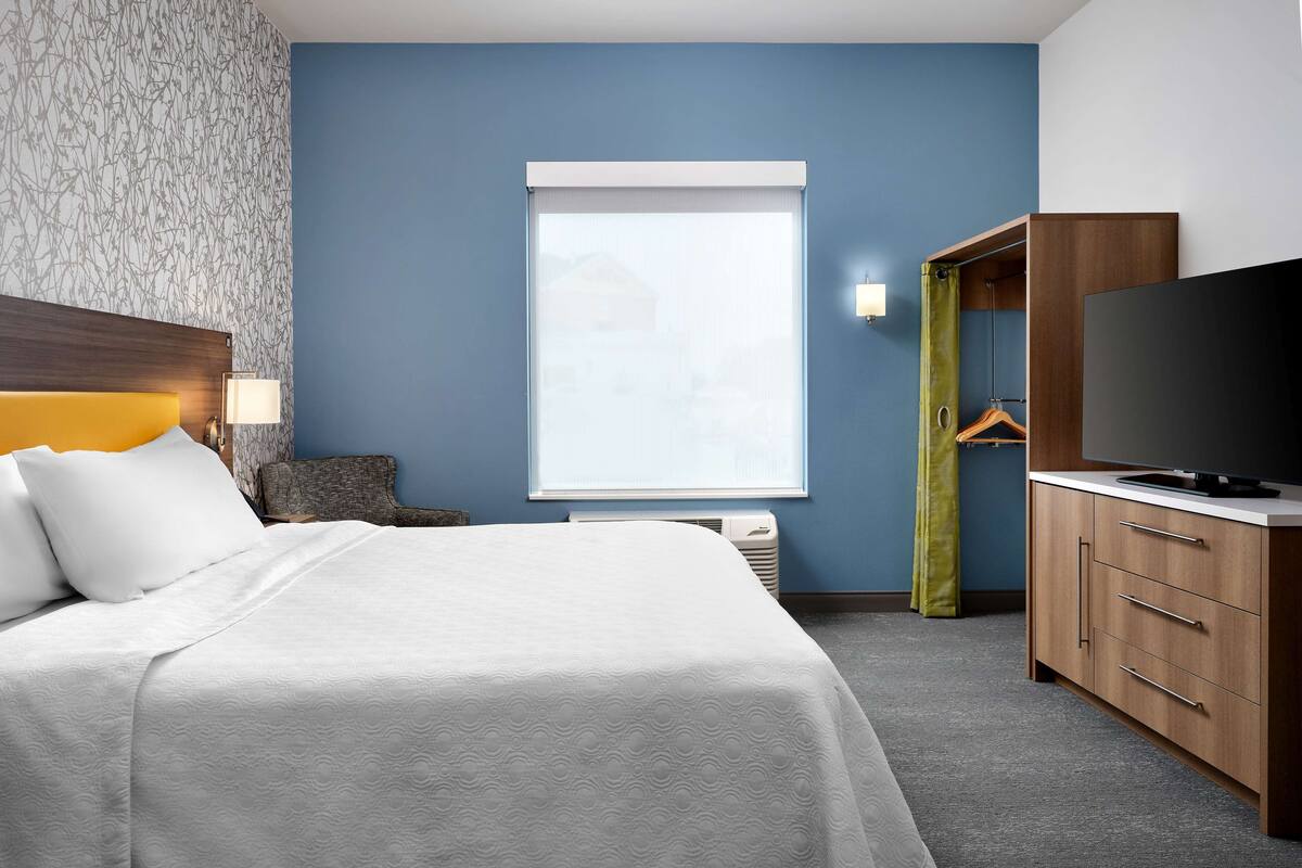 A hotel room with a bed, a television, a wardrobe, and a window with blinds.