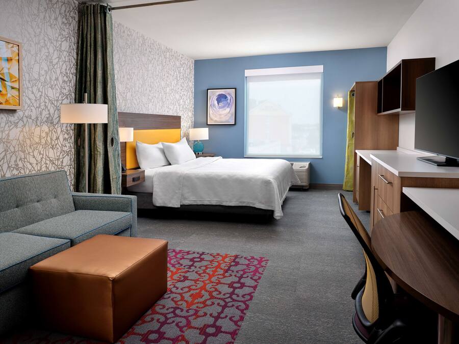 A hotel room with a bed, a sofa, a desk, and a television.