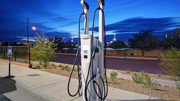 Una estación de carga pública para vehículos eléctricos, con una vista despejada del entorno, que incluye una carretera y edificios a lo lejos.