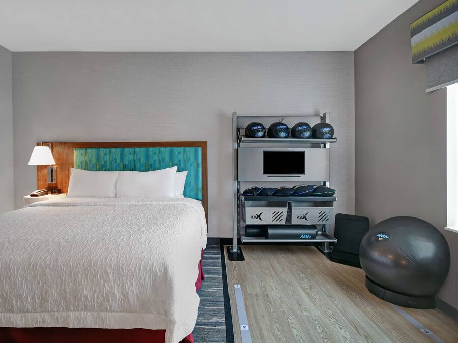 A hotel room with a bed, a TV, a shoe rack, and a fitness ball.