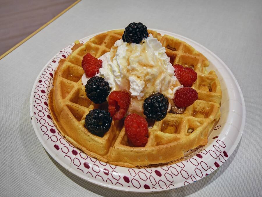 Un plato con un gofre belga cubierto de crema batida y frutos rojos frescos.