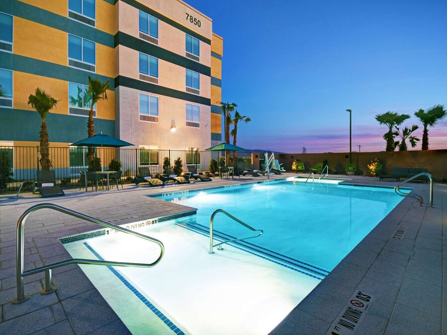 A hotel with a swimming pool, palm trees, and outdoor seating.