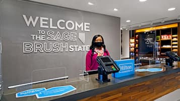 A hotel reception desk with a large welcome sign, a digital payment terminal, and a sign indicating the hotel's status as a Hilton Honors hotel.