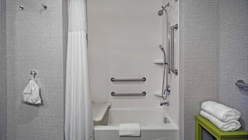 A modern bathroom with a walk-in shower, grab bars, a towel rack, and a green stool.