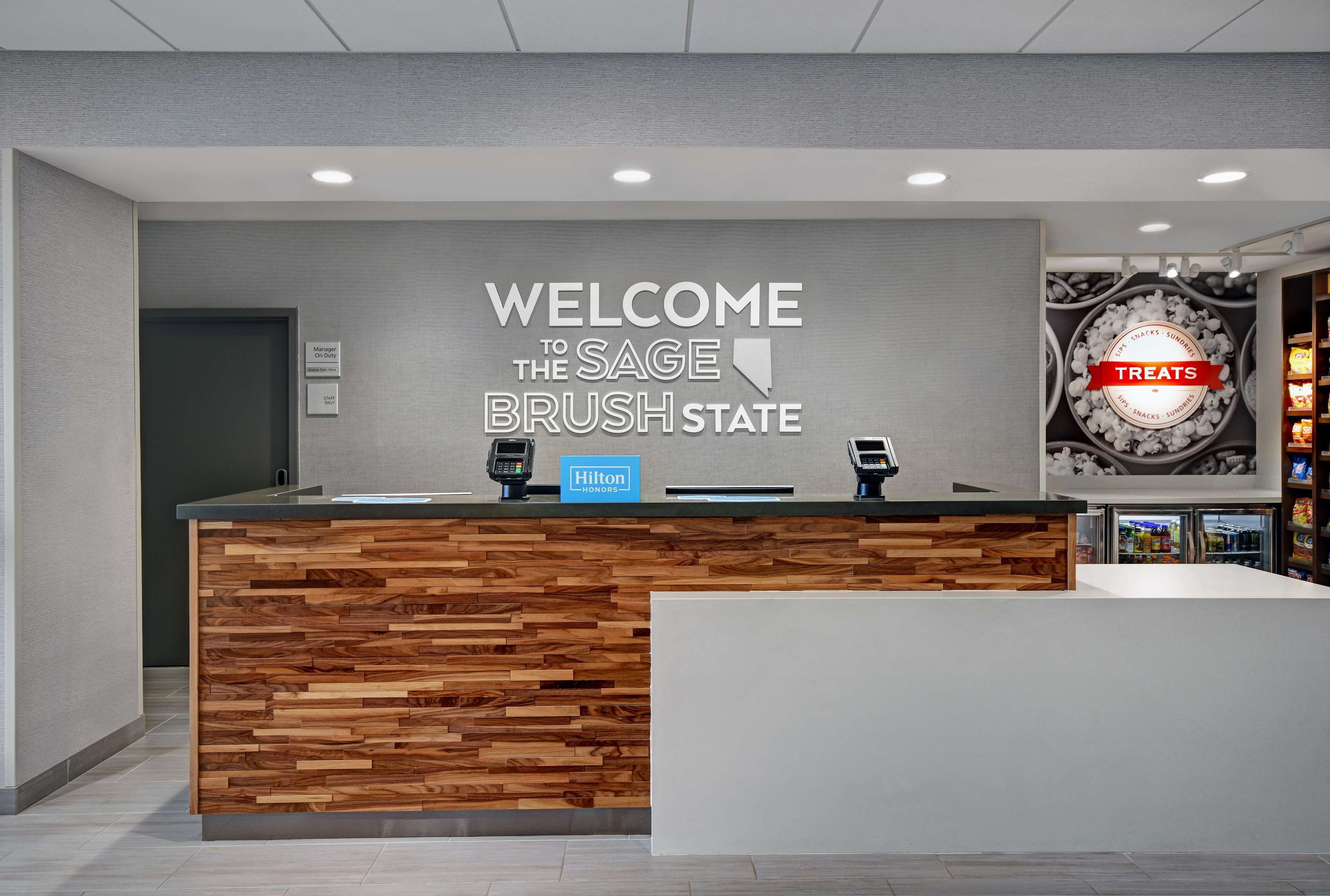 A reception desk with a sign reading "WELCOME TO THE SAGE BRUSH STATE" and a "Hilton" logo.
