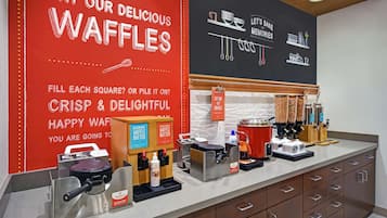 A waffle station with a red sign advertising waffles, a waffle maker, and a waffle batter dispenser.