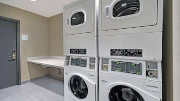 Une buanderie avec des machines à laver et des sèche-linge superposés, un évier blanc et une porte.