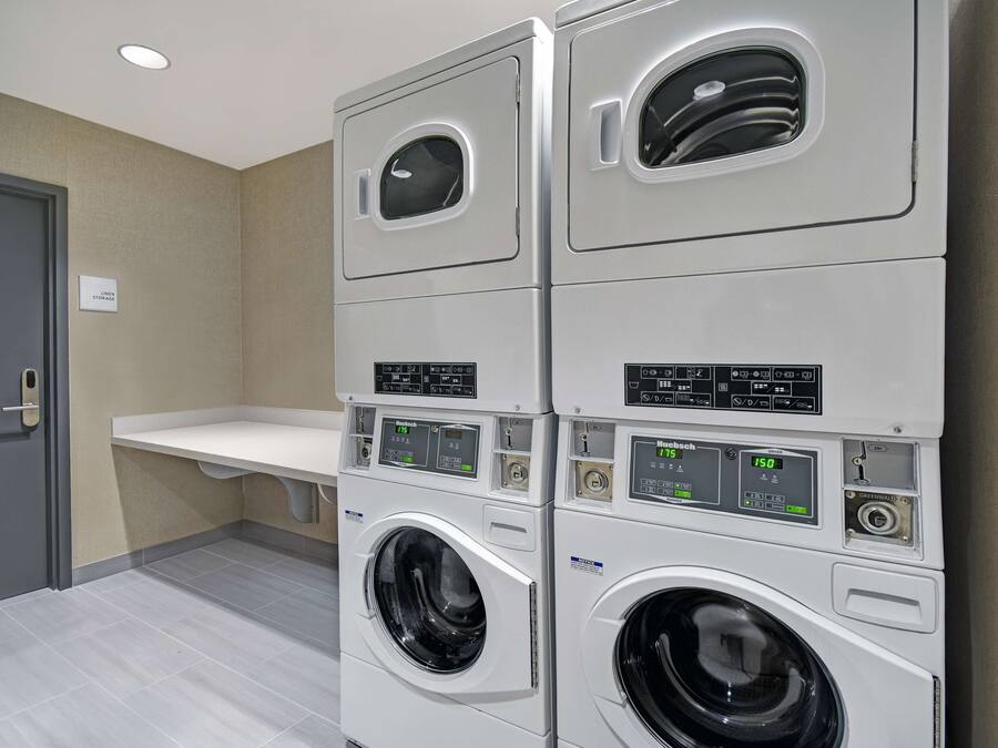 Une buanderie avec des machines à laver et des sèche-linge superposés, un évier blanc et une porte.