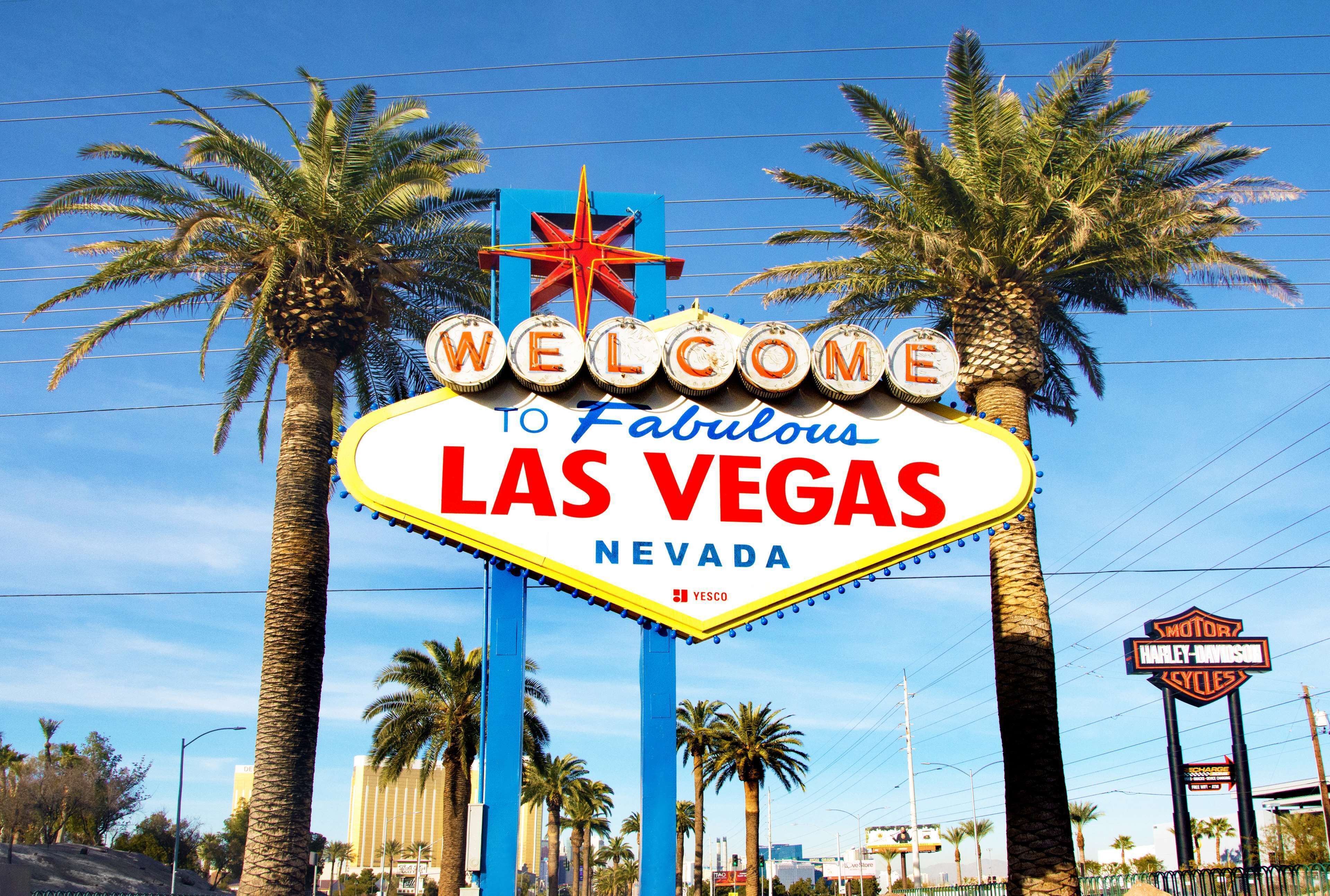 A neon sign welcoming visitors to Las Vegas, Nevada, with palm trees and a clear sky in the background.