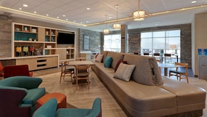En moderne hotellobby med en stor sofa, stole, et spiseområde og et køkken med et fjernsyn.