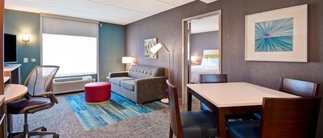 A hotel room with a large bed, a desk, a chair, a sofa, and a dining table.