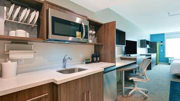 A modern kitchen with a built-in microwave, sink, and dishwasher. There is a seating area with a chair and a desk.