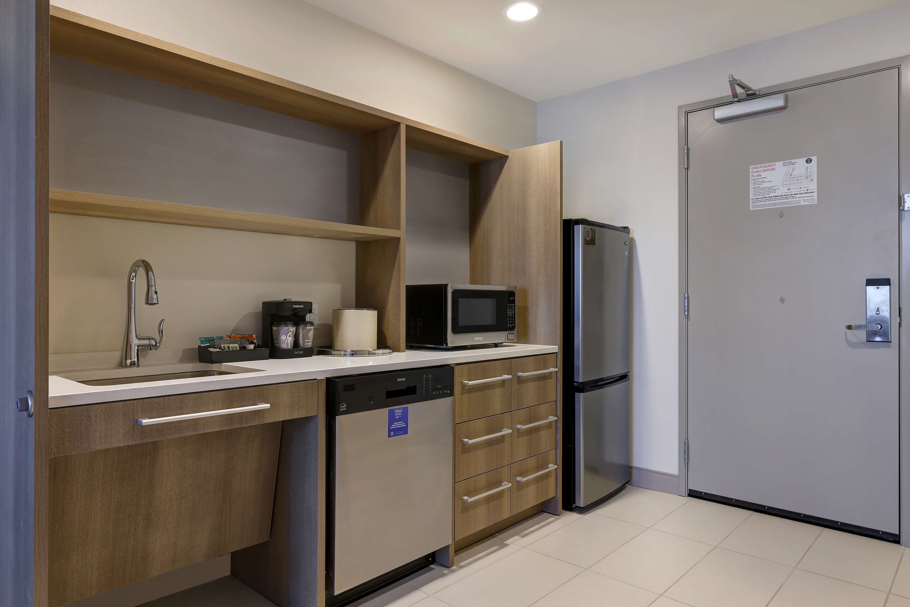 A modern kitchen with a dishwasher, microwave, refrigerator, and wooden cabinets.