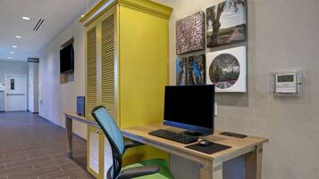 Een moderne kantoorruimte met een bureau, computer en stoel. Er hangen ingekaderde foto’s aan de muur en een thermostaat bevindt zich rechts.