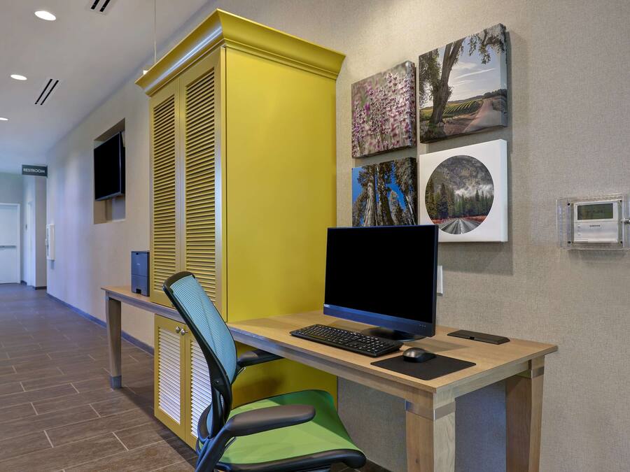 Een moderne kantoorruimte met een bureau, computer en stoel. Er hangen ingekaderde foto’s aan de muur en een thermostaat bevindt zich rechts.