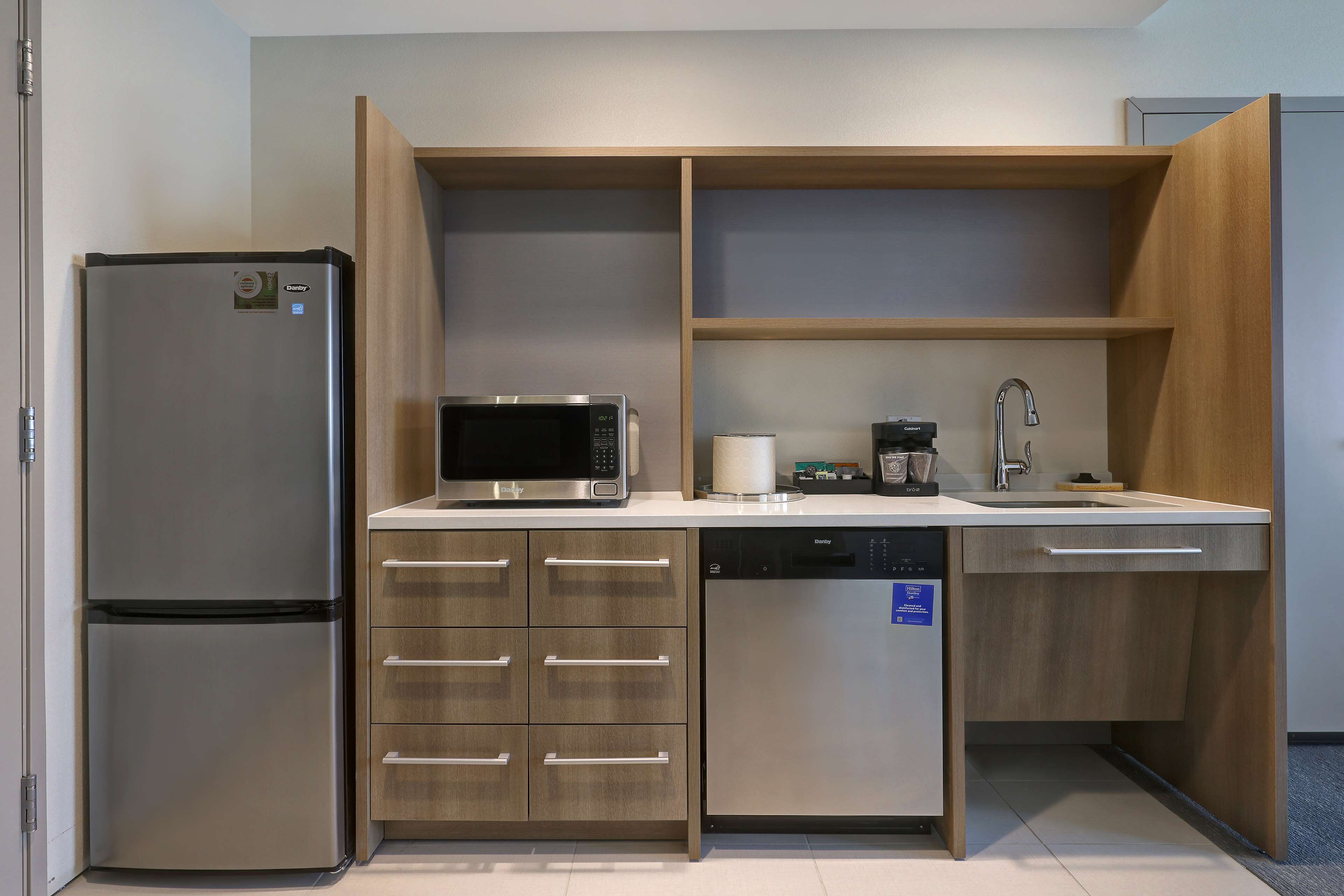 A compact kitchen with a built-in refrigerator, microwave, coffee maker, and dishwasher.