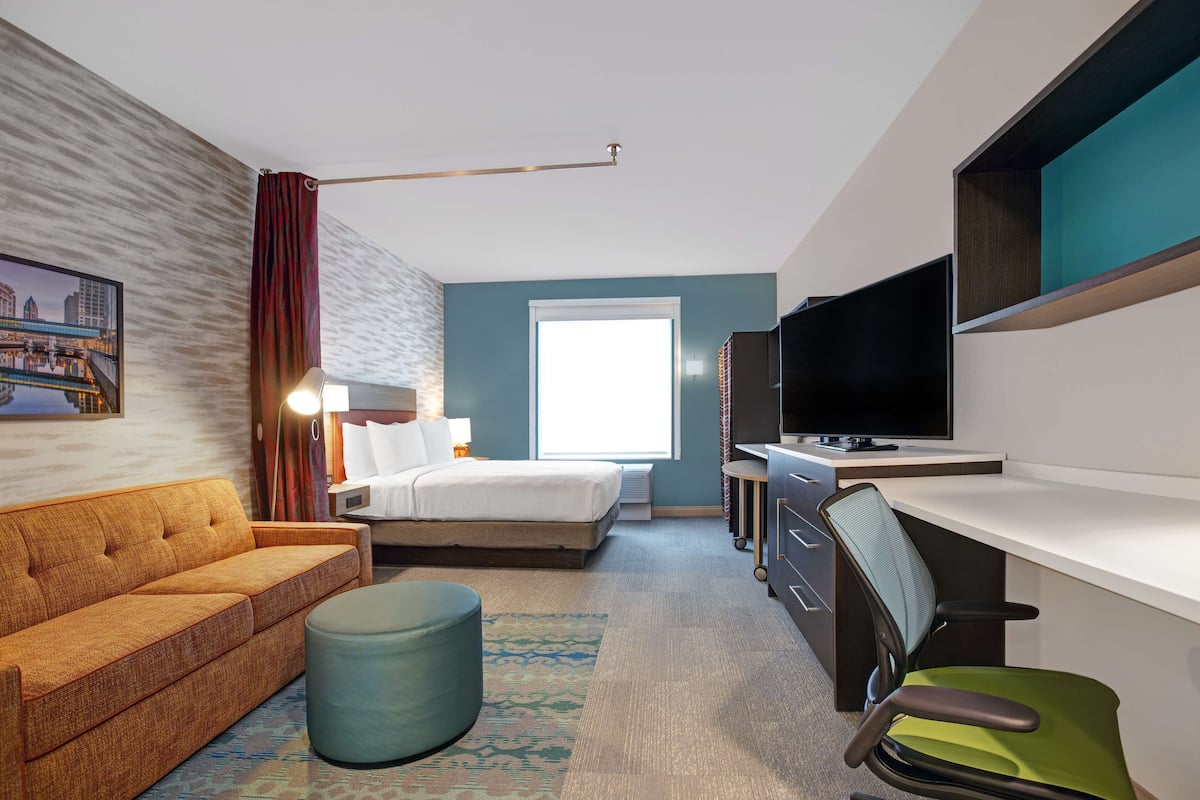 Een hotelkamer met een bed, een slaapbank, een bureau met stoel, een televisie en een raam.
