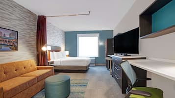 Habitación de hotel con cama, sofá, escritorio con silla, televisor y ventana.