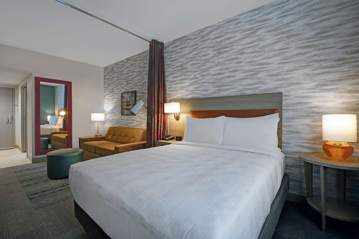 Een hotelkamer met een groot bed, een zithoek met een stoel, een kleine tafel en een spiegel.