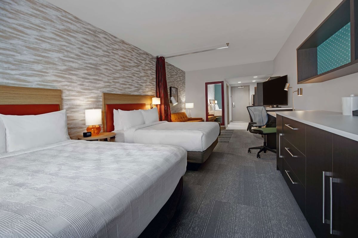 Een hotelkamer met twee bedden, een bureau, een televisie en een badkamer op de achtergrond.