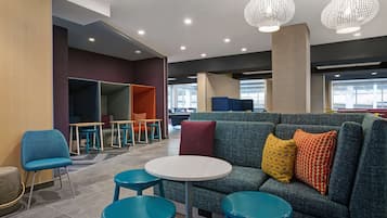Un espace de détente moderne comprenant un canapé, des fauteuils et une table, avec différents types d’assises et une grande fenêtre laissant entrer la lumière naturelle.