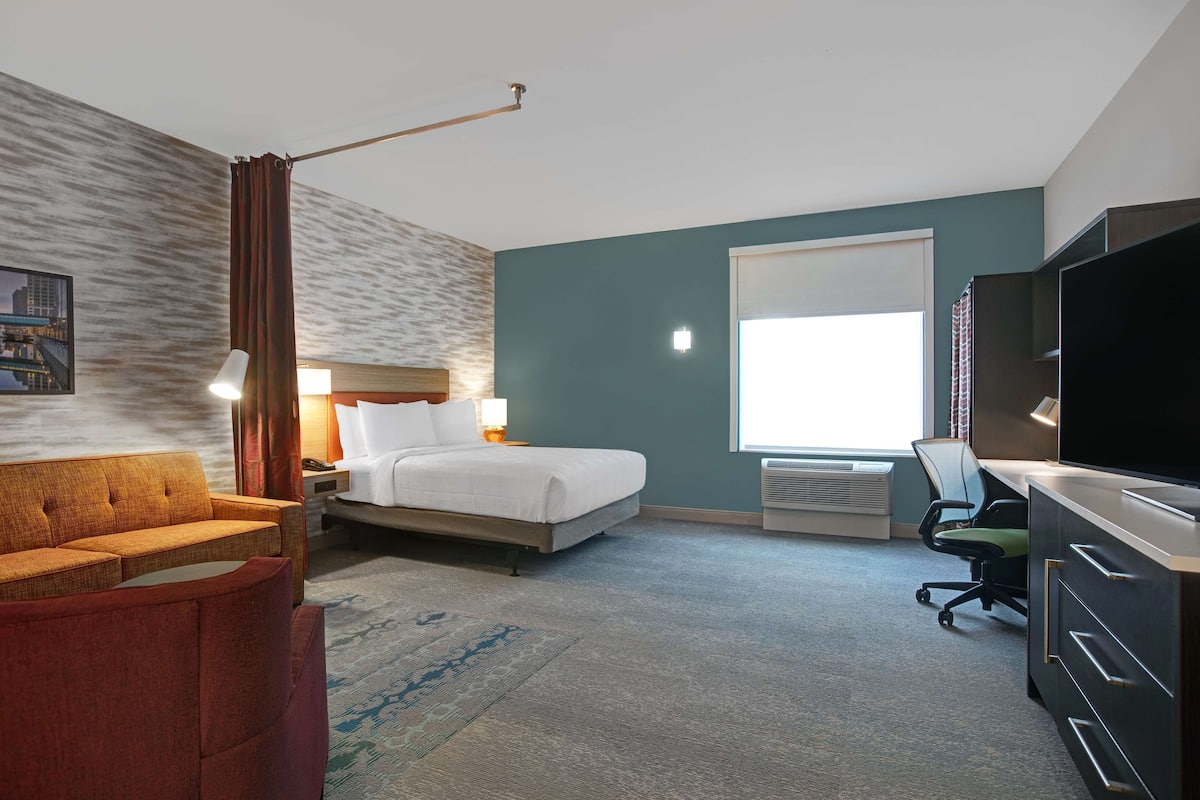 Hotelkamer met een bed, een bureau met stoel, een televisie, een bank en een groot raam.