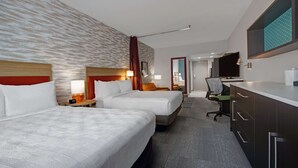 Habitación de hotel con dos camas, un escritorio, una silla, un televisor y un baño visible a través de una puerta abierta.