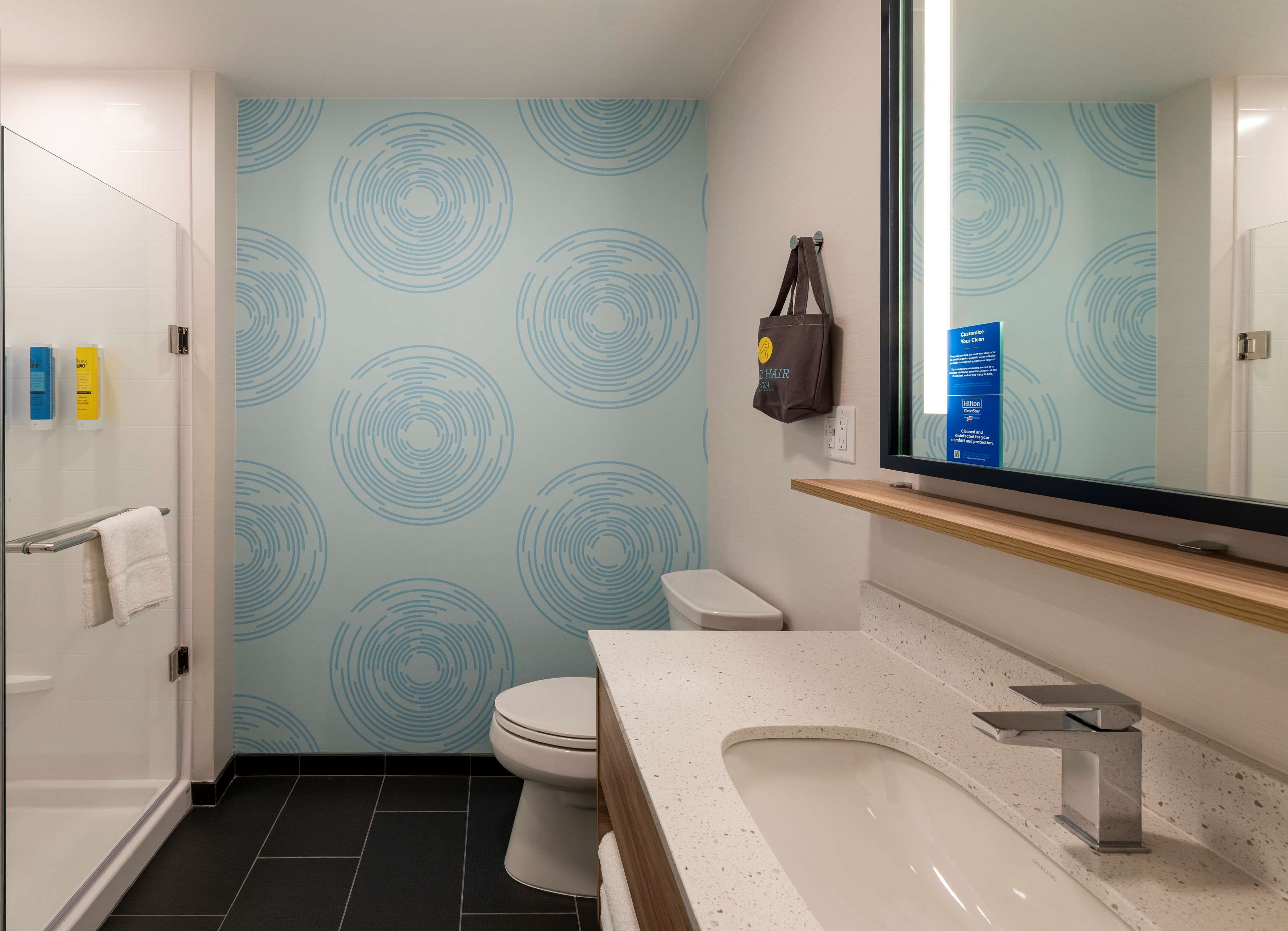 Ein modernes Badezimmer mit einem runden Muster an der Wand, einer Toilette, einem Waschbecken inklusive Spiegel und einem Handtuchhalter.