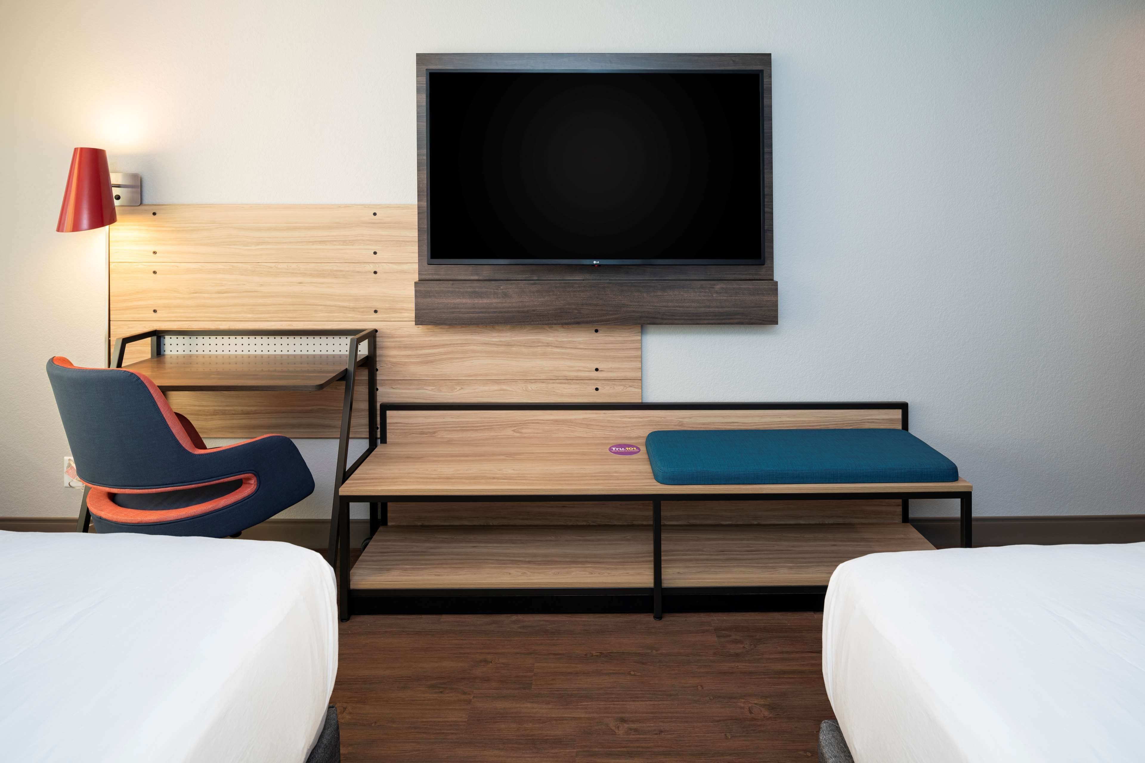 Quarto de hotel com televisão na parede, uma escrivaninha com cadeira e duas camas.
