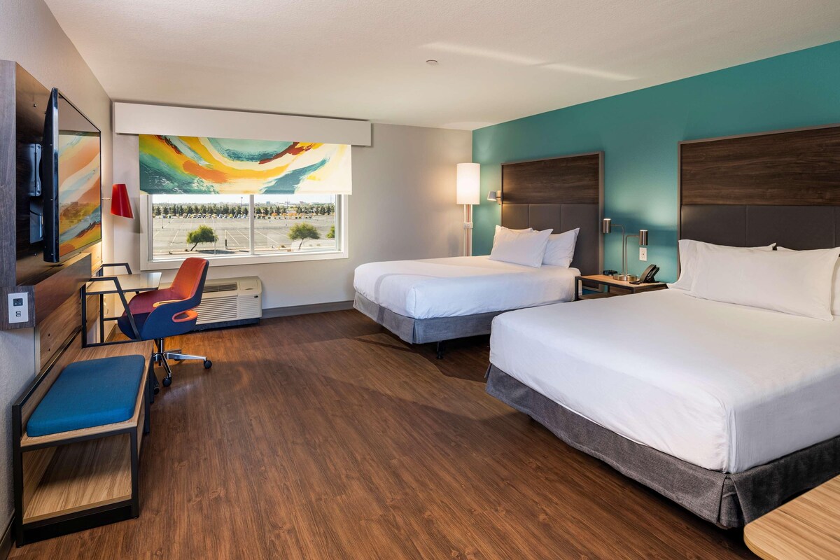 A hotel room with two beds, a desk, a chair, a TV, and a painting.