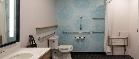 Un baño moderno con inodoro blanco, lavamanos con encimera moteada y espejo. Hay pasamanos en las paredes y una zona de ducha con cortina.